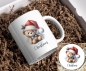 Preview: Weihnachtstasse mit niedlichem Teddybär-Motiv und passendem Untersetzer: Ein süßer Teddybär trägt eine rote Weihnachtsmütze mit Beeren und Stechpalmenblättern und eine kleine blaue Schleife um den Hals. Unter dem Motiv steht der Schriftzug ‚Merry Christma